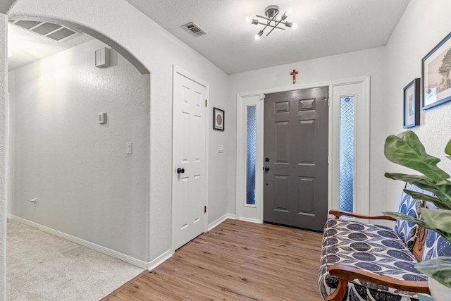 entrance foyer with light wood-style floors, baseboards, visible vents, and arched walkways