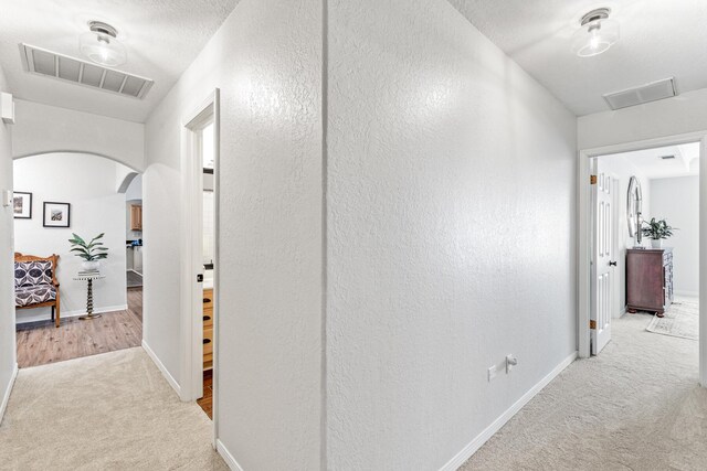 hallway with baseboards, visible vents, arched walkways, and carpet flooring