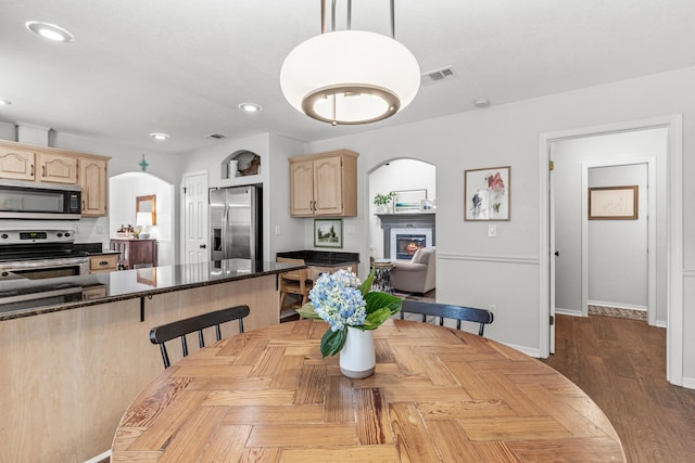 dining room featuring arched walkways, recessed lighting, visible vents, a glass covered fireplace, and baseboards