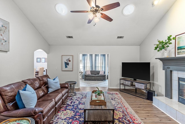 living area with arched walkways, visible vents, a tiled fireplace, and wood finished floors