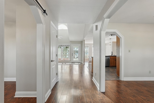 hallway with a sink, a barn door, dark wood finished floors, and baseboards