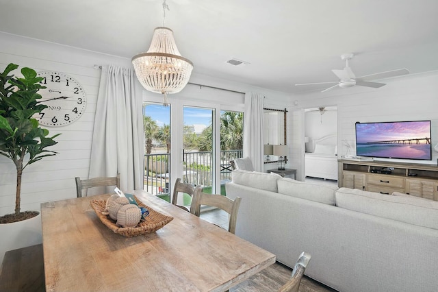 dining room featuring visible vents, wooden walls, and ceiling fan with notable chandelier