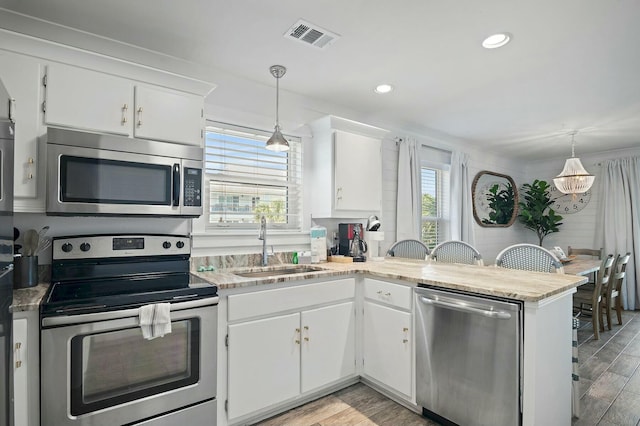 kitchen with appliances with stainless steel finishes, decorative light fixtures, a peninsula, and white cabinetry