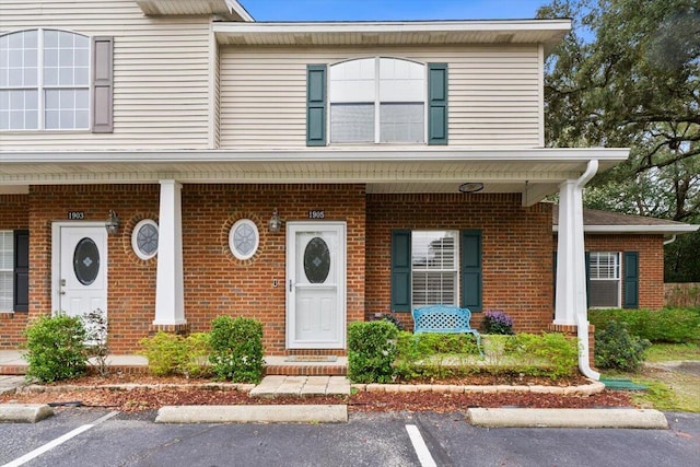 view of front of property featuring covered porch, uncovered parking, and brick siding