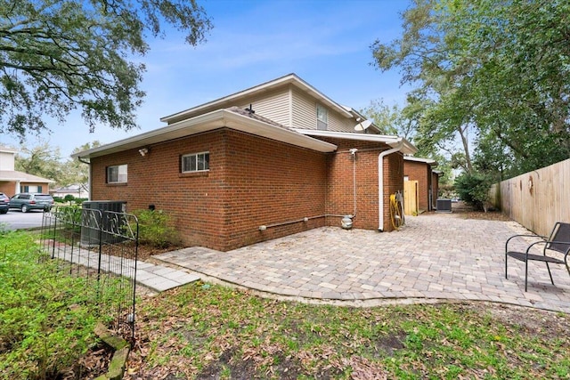 rear view of property featuring a patio, brick siding, central AC unit, and fence