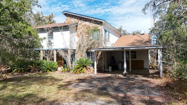 back of house featuring stone siding and a lawn