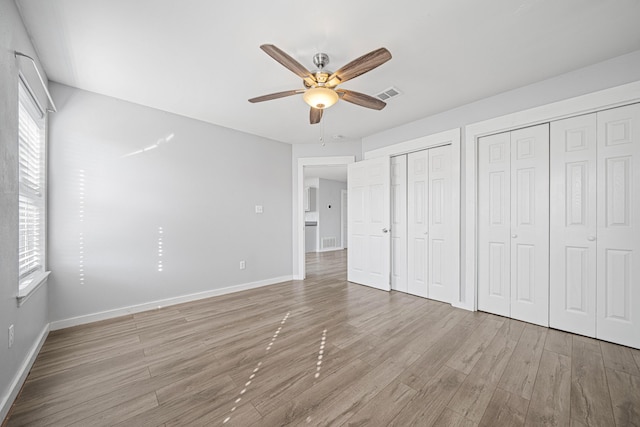 unfurnished bedroom featuring a ceiling fan, visible vents, baseboards, light wood-type flooring, and two closets