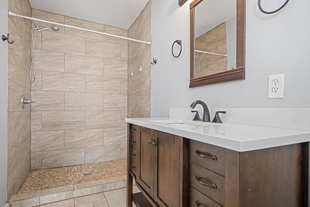 full bathroom with tiled shower, vanity, and a textured ceiling