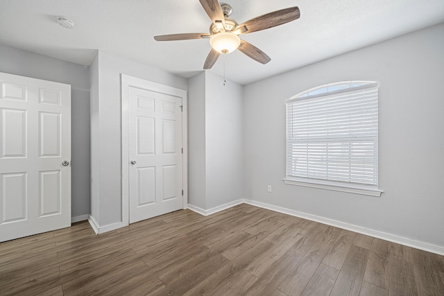 unfurnished bedroom with ceiling fan, a textured ceiling, baseboards, and wood finished floors