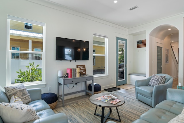 living room featuring arched walkways, light wood-style flooring, recessed lighting, visible vents, and ornamental molding