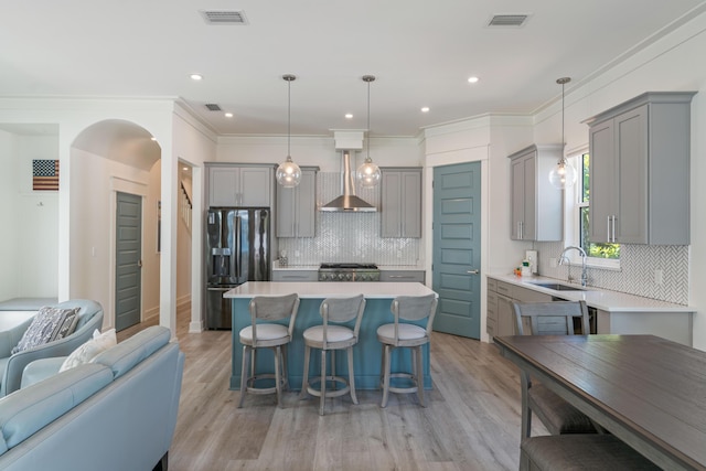 kitchen featuring a sink, light countertops, wall chimney exhaust hood, black refrigerator with ice dispenser, and pendant lighting