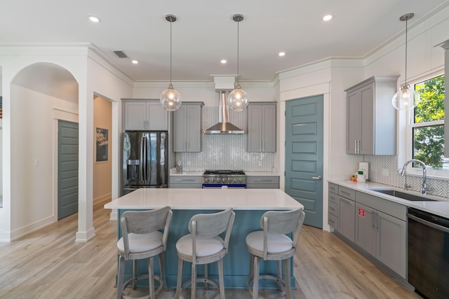 kitchen with a sink, light countertops, wall chimney range hood, black fridge, and high end stainless steel range