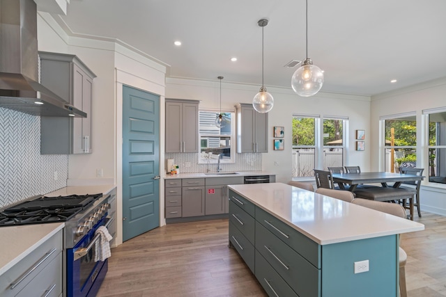 kitchen with wall chimney exhaust hood, a center island, high end stainless steel range oven, light countertops, and pendant lighting