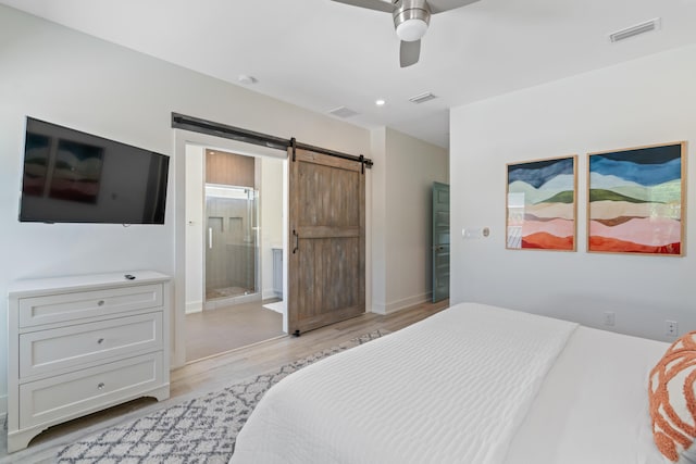 bedroom featuring a barn door, visible vents, light wood-style flooring, and connected bathroom