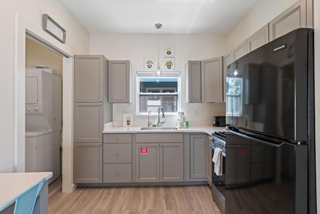 kitchen featuring stacked washer / drying machine, freestanding refrigerator, light countertops, pendant lighting, and a sink