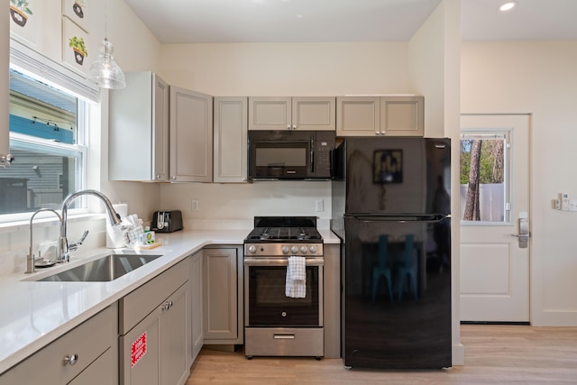 kitchen with a sink, black appliances, light countertops, and pendant lighting