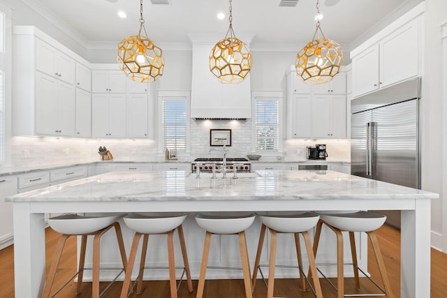 kitchen featuring decorative light fixtures, a breakfast bar area, white cabinets, light stone countertops, and a large island with sink