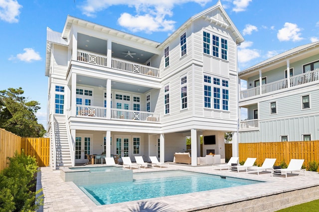 back of property with a warm lit fireplace, a balcony, fence, a patio area, and a pool with connected hot tub