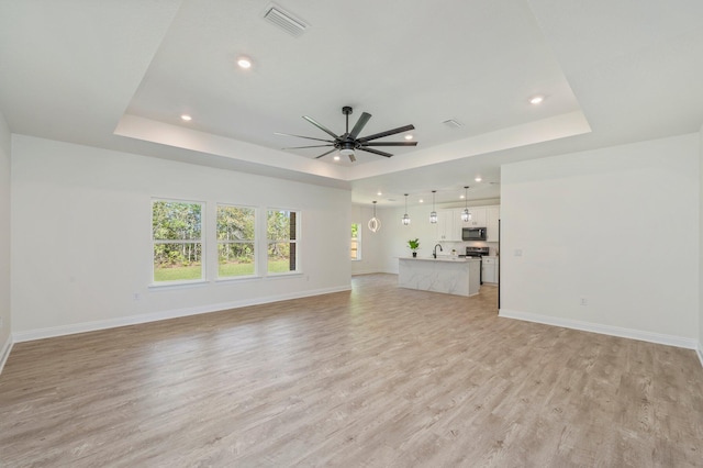 unfurnished living room with light wood finished floors, baseboards, and a raised ceiling