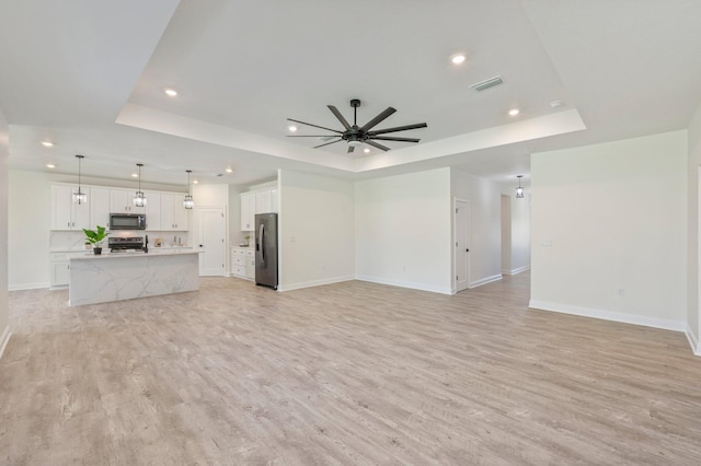 unfurnished living room featuring a tray ceiling, visible vents, and light wood-style floors