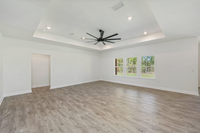 empty room featuring light wood finished floors, a tray ceiling, and baseboards