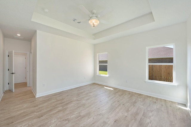 spare room with light wood-style floors, baseboards, a raised ceiling, and a ceiling fan