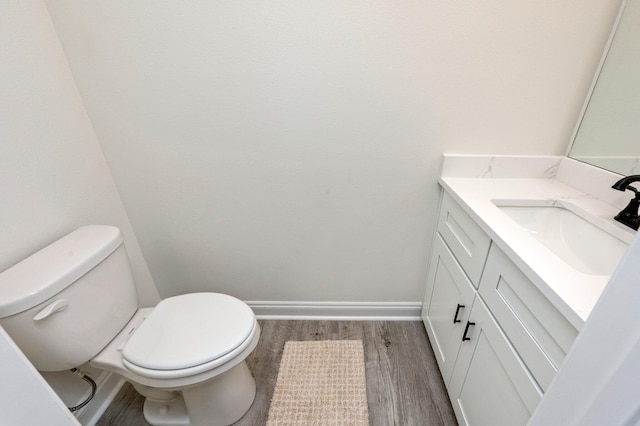 half bath featuring baseboards, vanity, toilet, and wood finished floors