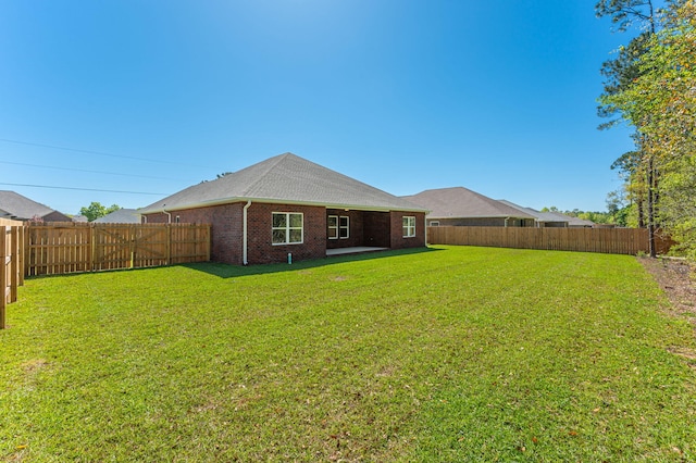 rear view of house featuring brick siding, a lawn, and a fenced backyard