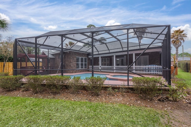 rear view of property with glass enclosure, brick siding, fence, a pool with connected hot tub, and a yard