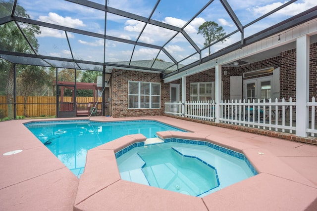 view of pool featuring glass enclosure, a pool with connected hot tub, a patio area, and fence