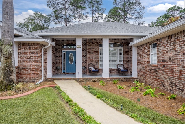 property entrance with covered porch, brick siding, roof with shingles, and a lawn