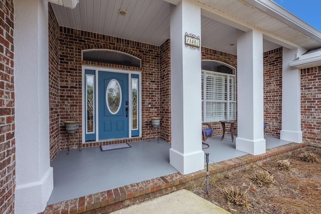 view of exterior entry with covered porch and brick siding