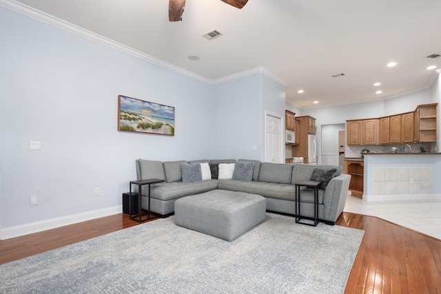 living area with baseboards, visible vents, ornamental molding, light wood-type flooring, and recessed lighting