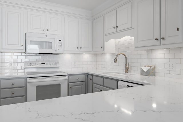 kitchen with light stone countertops, white appliances, a sink, white cabinets, and decorative backsplash