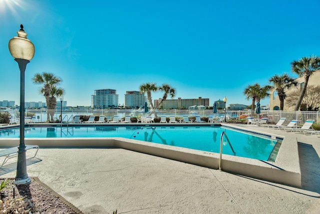 community pool with a patio, fence, and a city view