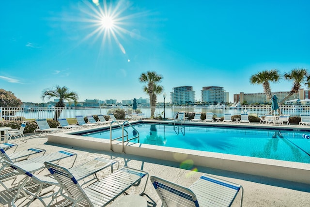 pool featuring a patio, a water view, fence, and a city view