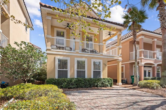 view of front facade featuring a ceiling fan, a tiled roof, a balcony, and stucco siding