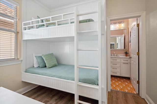 bedroom featuring a sink, baseboards, ornamental molding, dark wood-style floors, and ensuite bath