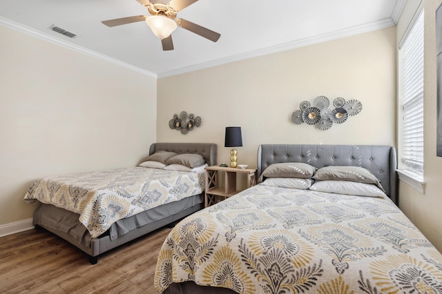 bedroom featuring wood finished floors, a ceiling fan, baseboards, visible vents, and crown molding