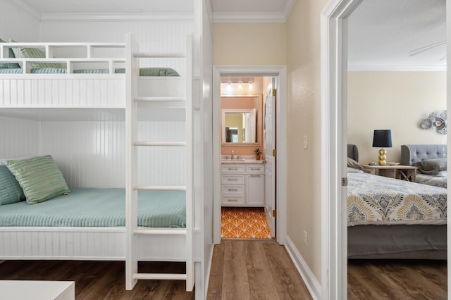 bedroom with crown molding, connected bathroom, a sink, wood finished floors, and baseboards