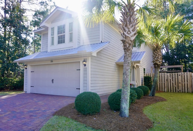 view of front facade with an attached garage, fence, metal roof, and decorative driveway