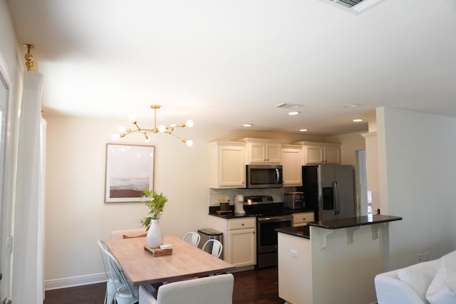 kitchen featuring a notable chandelier, stainless steel appliances, dark countertops, decorative backsplash, and a kitchen bar