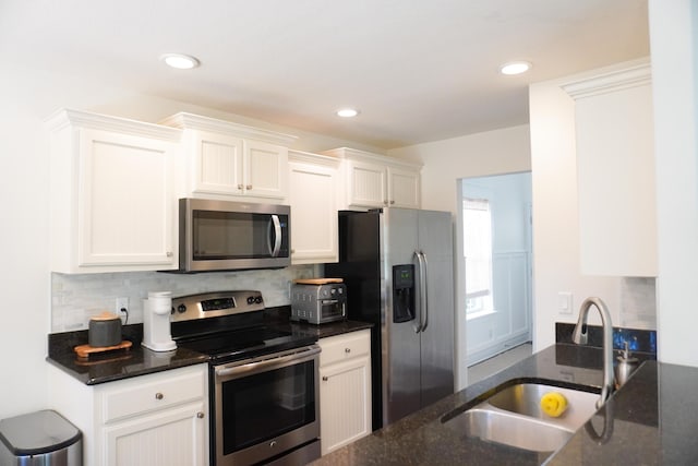 kitchen featuring tasteful backsplash, dark stone counters, stainless steel appliances, white cabinetry, and a sink