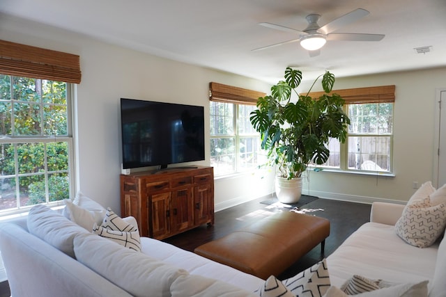 living room featuring a healthy amount of sunlight, ceiling fan, baseboards, and dark wood-type flooring