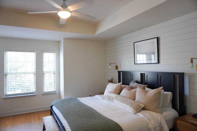 bedroom with wooden walls, a ceiling fan, baseboards, light wood finished floors, and a raised ceiling