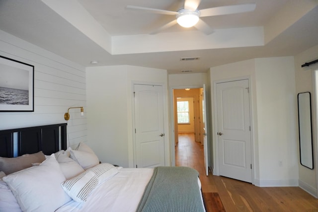 bedroom featuring a tray ceiling, visible vents, baseboards, and wood finished floors