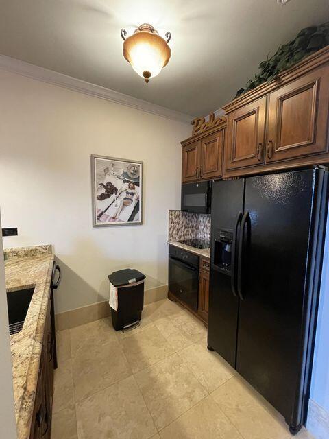 kitchen featuring light stone counters, baseboards, ornamental molding, backsplash, and black appliances