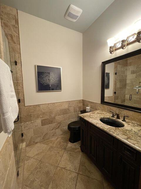 bathroom with tile walls, toilet, wainscoting, a shower stall, and vanity