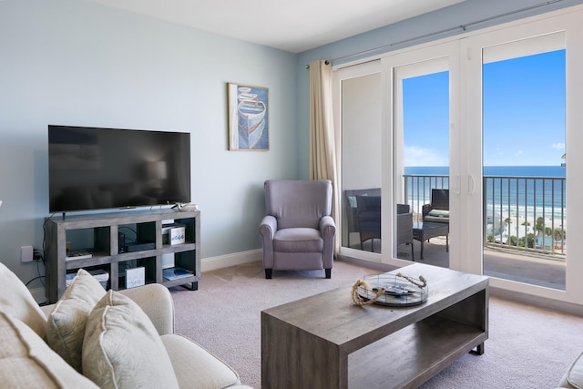 carpeted living area with a view of the beach, a water view, and baseboards