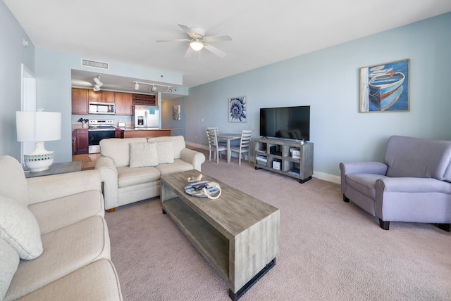 living area featuring baseboards, rail lighting, a ceiling fan, and light colored carpet